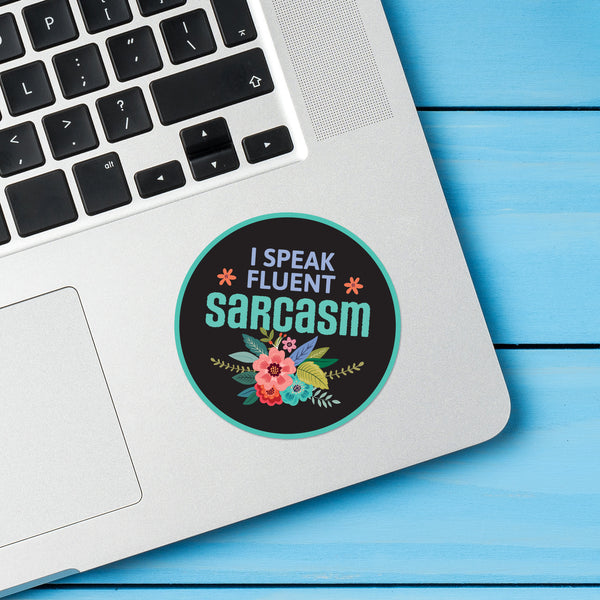 Laptop with a round sticker reading 'I speak fluent sarcasm' on a blue wooden surface
