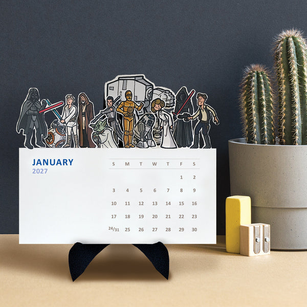 Illustrations of a variety of Star Wars characters on top of each monthly card on a desktop calendar on a black easel sitting on a table.