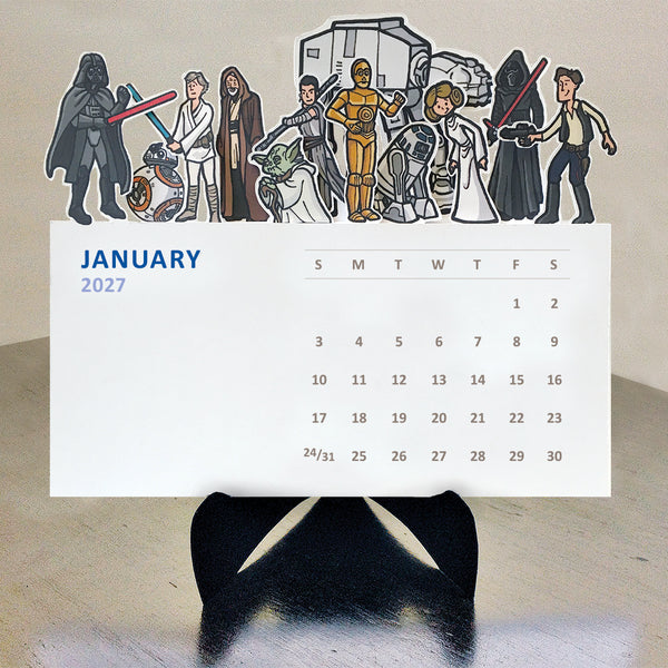 Illustrations of a variety of Star Wars characters on top of each monthly card on a desktop calendar on a black easel sitting on a table.
