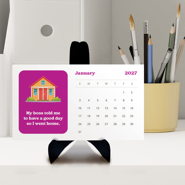 An adulting desk calendar for 2027 shown against a neutral background, featuring a bright pink block with a cartoon house and the text 'My boss told me to have a good day so I went home.' Calendar is sitting on a black easel.