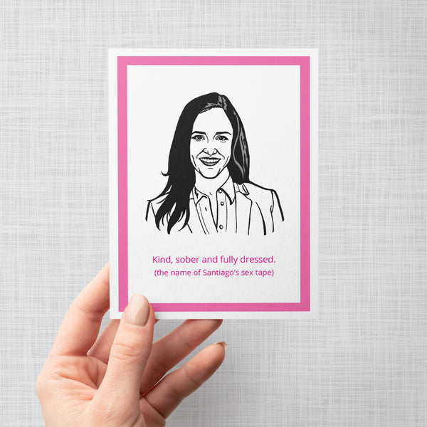 A hand holding a greeting card featuring a black and white line art portrait of Brooklyn Nine Nine's Amy Santiago with the text 'Kind, sober and fully dressed. (the name of Santiago's sex tape)' in pink, framed by a bright pink border on a white background, set against a light gray backdrop.