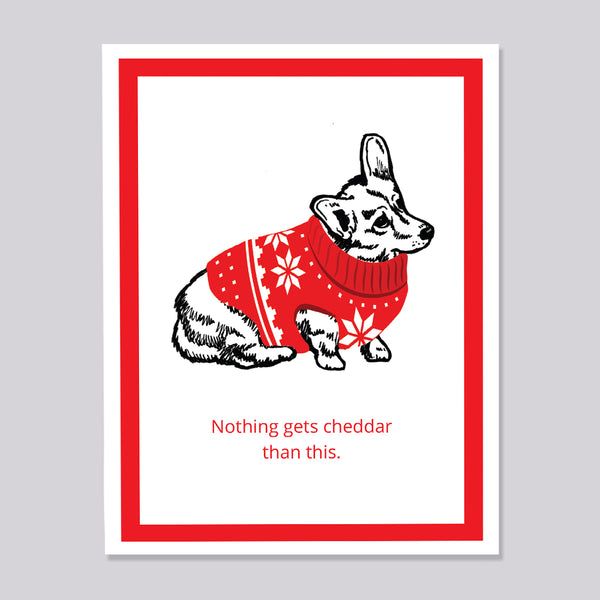 A white greeting card with a red border, featuring Brooklyn Nine Nine's cheddar dog wearing a red holiday sweater with white snowflake patterns. The card has the text 'Nothing gets cheddar than this.