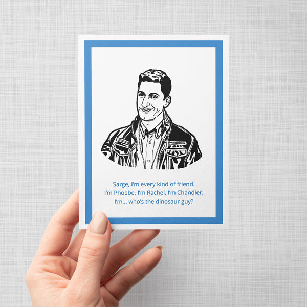 A hand holding a greeting card featuring a black and white comic-style illustration of Brooklyn Nine Nine's Jake Peralta wearing a leather jacket, with blue text below reading, 'Sarge, I'm every kind of friend. I'm Phoebe, I'm Rachel, I'm Chandler. I'm... who's the dinosaur guy?'