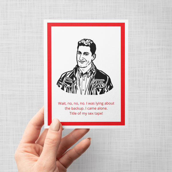 A hand holding a greeting card featuring a black and white illustration of Brooklyn Nine Nine's Jake Peralta in a leather jacket, with red text below that reads, 'Wait, no, no, no. I was lying about the backup. I came alone. Title of my sex tape!'