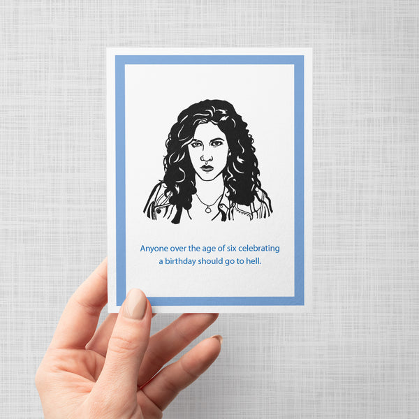 A hand holding a greeting card with an illustration of Rosa Diaz from Brooklyn Nine Nine, with a text on the card that reads 'Anyone over the age of six celebrating a birthday should go to hell.'.