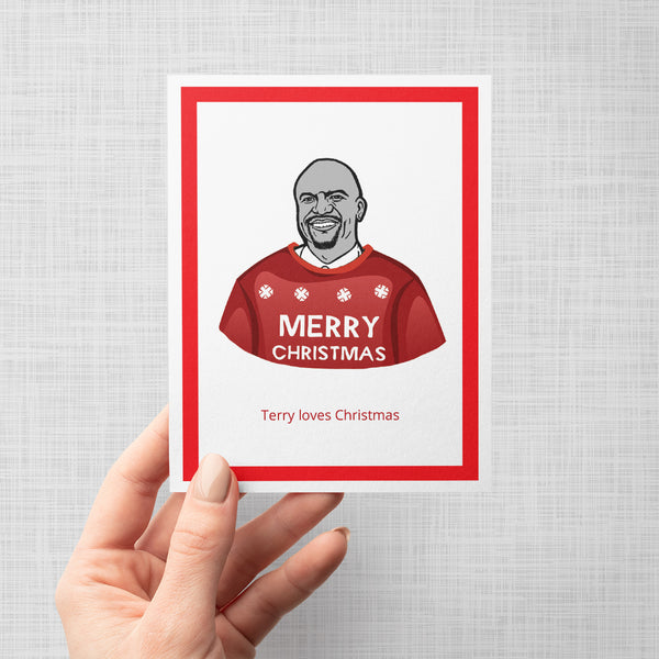 A hand holding a Christmas greeting card featuring an illustration of Brooklyn Nine Nine's Terry wearing a red sweater with snowflakes and the words 'MERRY CHRISTMAS'. Below the illustration, the text reads 'Terry loves Christmas'.