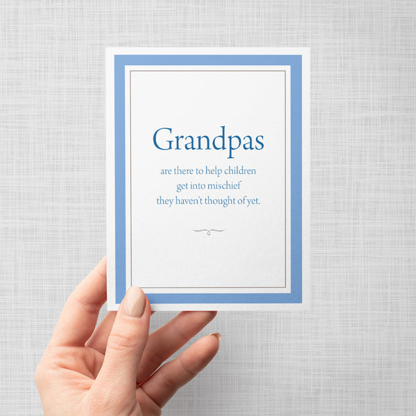 Hand holding greeting card with text 'Grandpas are there to help children get into mischief they haven't thought of yet'