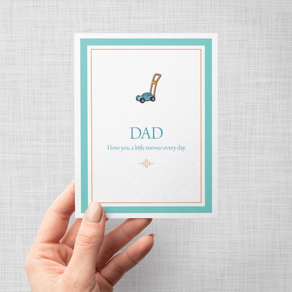 Hand holding greeting card with a lawn mower illustration and text 'Dad I love you a little mower every day'