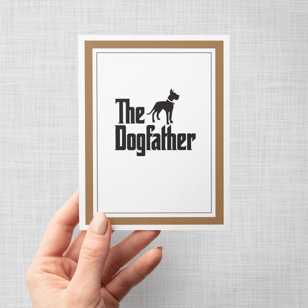 Hand holding greeting card with dog silhouette illustration and text 'The Dogfather'
