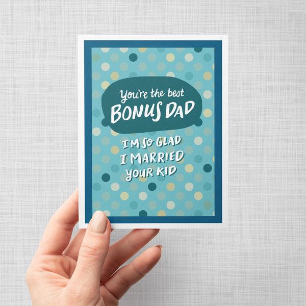Hand lettered greeting card with text 'You're the best BONUS DAD I'm so glad I married your kid' on a blue polka dot background.