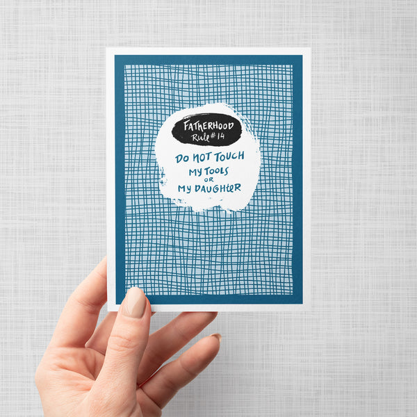 Greeting card with blue grid pattern and humorous text 'fatherhood rule 14. Do not touch my tools or my daughter'.
