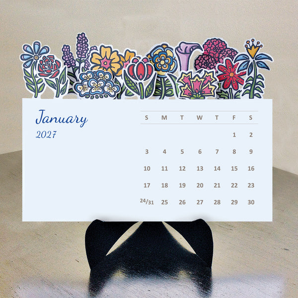 A 2027 desk calendar with colorful floral illustrations along the top, displayed on a black stand against a beige background.