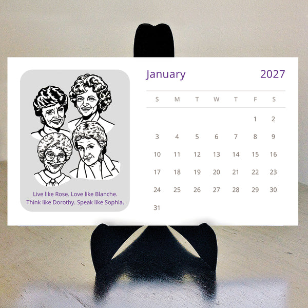 A white monthly 2027 calendar with black and white illustration of the Golden Girls characters displayed on a black stand against a beige wall and floor. 