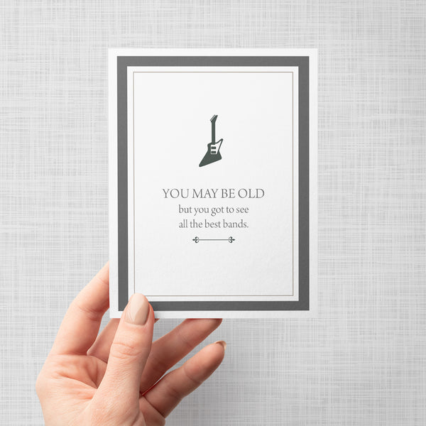 Hand holding greeting card with guitar silhouette and humorous text 'You may be old but you got to see all the best bands'