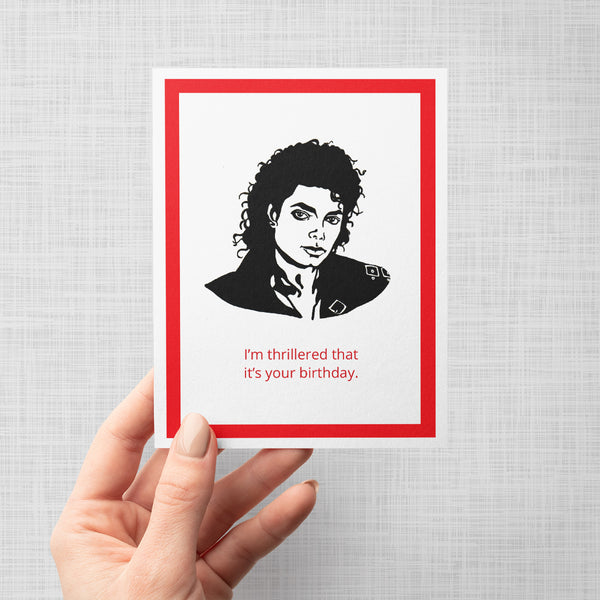 Hand holding a greeting card with Michael Jackson illustration and text 'I'm thrillered that it's your birthday'