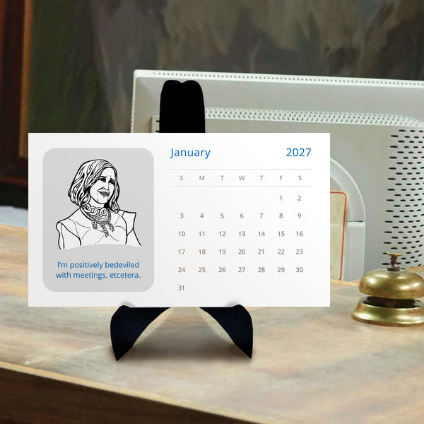 A Schitts Creek 2027 desk calendar displayed on a black stand against a beige wall. The calendar features a gray square with a black-and-white line drawing of Moira Rose and the text 'I'm positively bedeviled with meetings, etcetera.' displayed on a desk.