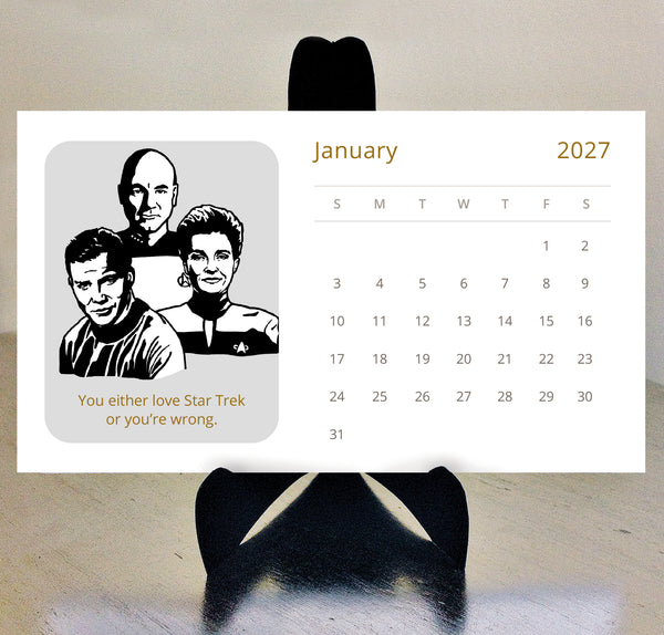 A 2027 Star Trek desk calendar featuring a black-and-white Star Trek captains illustration and the phrase 'You either love Star Trek or your wrong,' displayed on a black stand against a light beige wall.