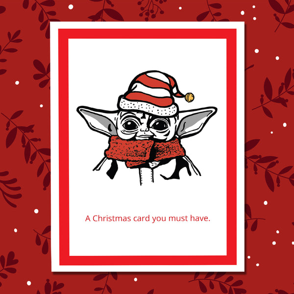 A Christmas-themed greeting card featuring a cartoon illustration of Grogu wearing a red and white Santa hat and matching red scarf, with the text 'A Christmas card you must have.' printed below on a red Christmas background.