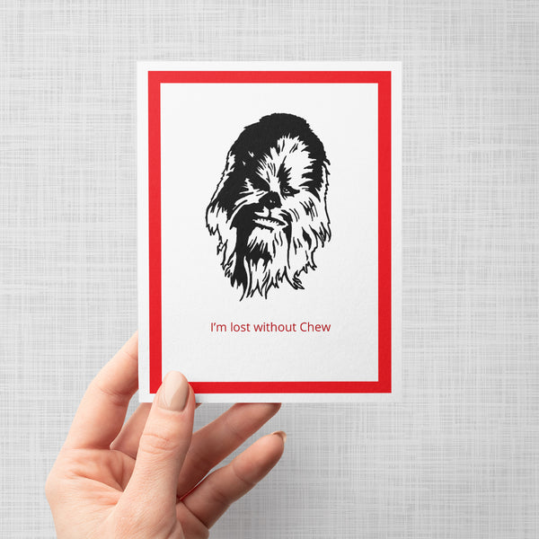 A hand holding a greeting card featuring a black line-art illustration of Chewbacca's face with the red text 'I 'CHEW 'SE YOU' underneath, framed by a bold red border on a white background, shown against a light gray backdrop.