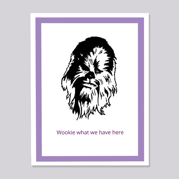 A greeting card featuring a black line art illustration of Chewbacca on a white background, framed by a double purple border. Below the illustration, the text 'Wookie what we have here' is written in purple.