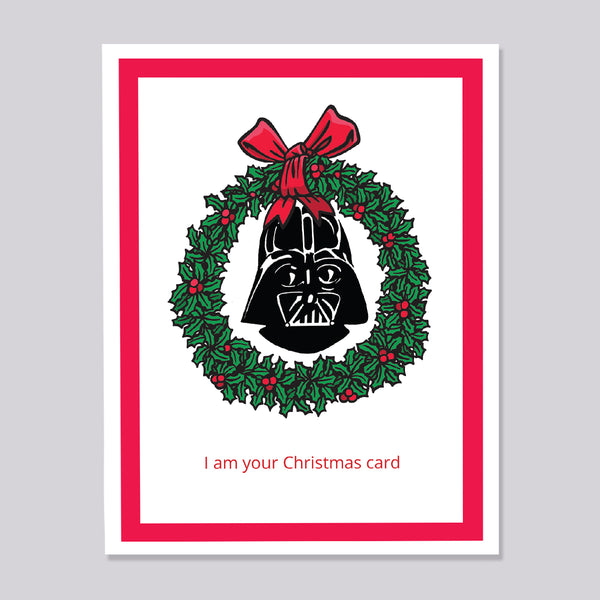A Christmas greeting card featuring Darth Vader's helmet inside a green holly wreath with a red bow, on a white card with a red border and the text 'I am your Christmas card' at the bottom.