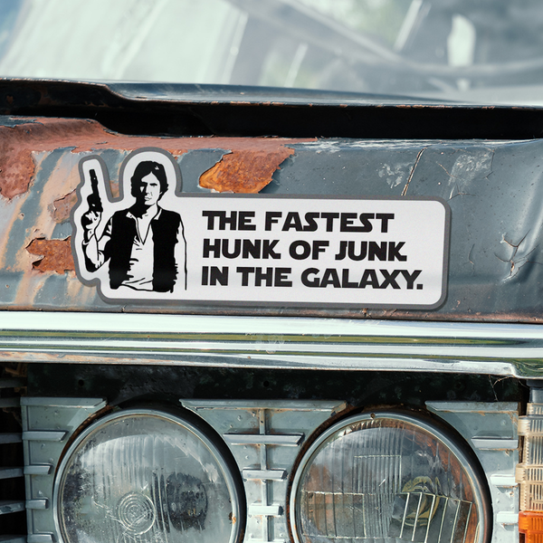 A die-cut vinyl bumper sticker featuring a black and white graphic of Star Wars Han Solo holding a gun next to the text 'THE FASTEST HUNK OF JUNK IN THE GALAXY.' applied to the front bumper of a rusted car.