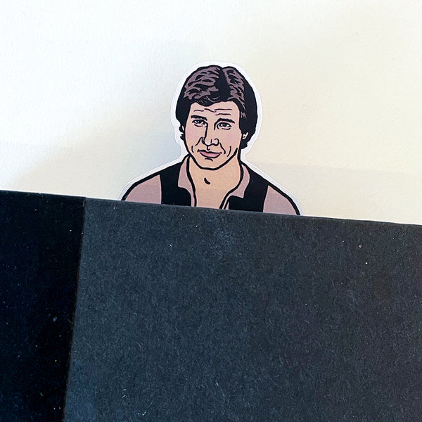 Illustration of Star Wars Han Solo on a die cut bookmark where arms over the front of a book page and the head peeks out the top.