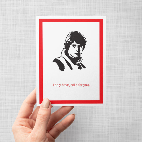 A hand holding a greeting card featuring a black-and-white portrait of Luke Skywalker with a red border and the text 'I only have Jedi-s for you.' in red at the bottom, shown against a light gray background.