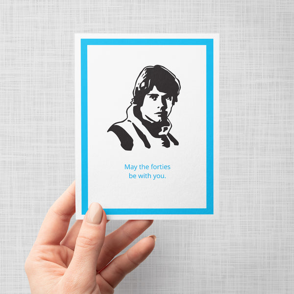 A hand holding a greeting card featuring a black-and-white portrait of Luke Skywalker with the text 'May the forties be with you.' in light blue below on a gray background.
