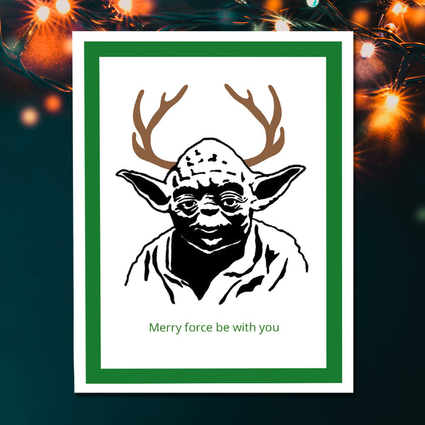 A greeting card featuring a stylized black-and-white portrait of Yoda with brown antlers and green text reading 'Merry force be with you' at the bottom, framed by a green border on a white print background against a Christmas lights  backdrop.